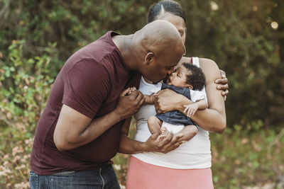 Young father kissing newborn daughter while mother holds her