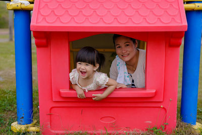 Portrait of woman with daughter in red dollhouse at playground