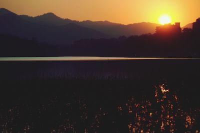 Scenic view of lake by silhouette mountains against orange sky