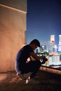 Young man crouching on building terrace at night