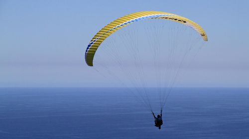 Person paragliding over sea against sky