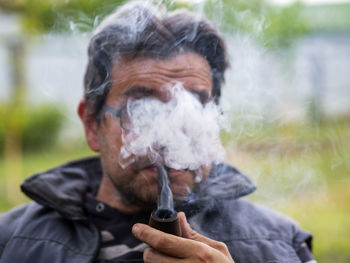 Unshaven caucasian man in glasses smokes a pipe