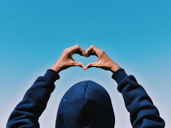 Low section of man holding heart shape against clear blue sky
