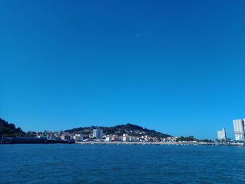 Sea by buildings against clear blue sky