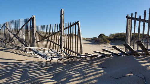 Shadow of railing on beach against clear blue sky