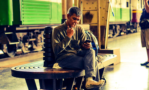 Full length of man using phone while sitting at railroad station