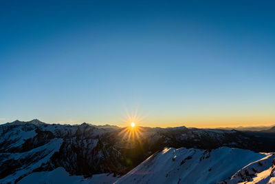 Scenic view of snow covered mountains against bright sun