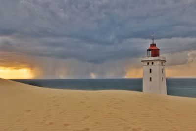 Lighthouse on beach against cloudy sky