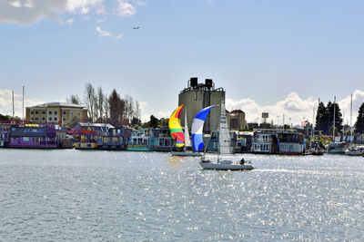 Sailboats in river by buildings in city against sky