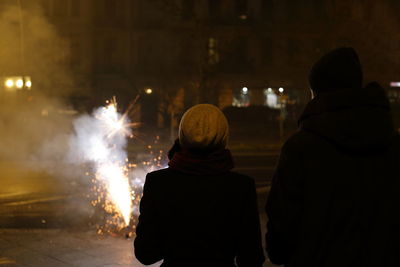 Rear view of people watching firework display at night