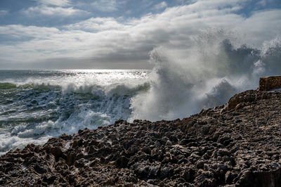 Waves breaking on rocks against sky