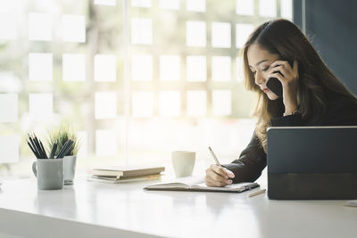 Young woman using mobile phone while sitting on table