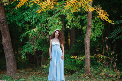 Portrait of woman standing by tree in forest