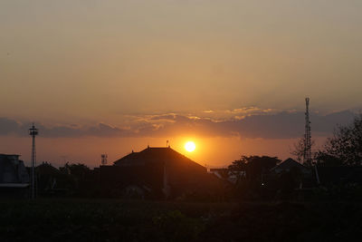 Silhouette buildings on field against sky during sunset