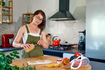 Woman making healthy breakfast or brunch, spreading peanut butter on a puffed corn cakes.