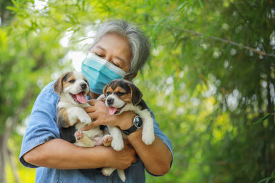 Senior woman wearing mask holding puppies standing outdoors