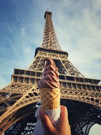 Low angle view of hand holding tower against cloudy sky