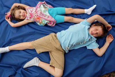 Directly above shot of siblings relaxing on blue fabric at field