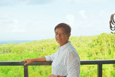 Portrait of smiling young woman standing on field against sky