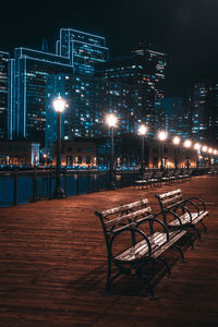 Empty benches on promenade against illuminated buildings at night