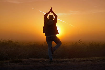 Silhouette man standing on grass against orange sky