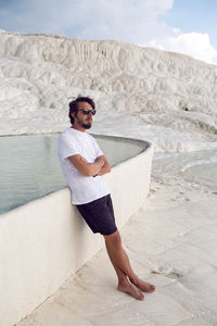 Man with a beard in a white t-shirt and shorts rest on a white mountain in pamukkale