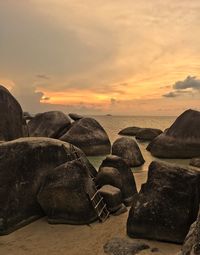 Rocks on beach against sky during sunset