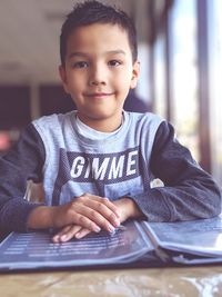 Portrait of smiling boy with menu on table sitting in restaurant