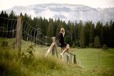 Full length of woman sitting on fence over field