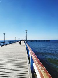 Pier over sea against clear blue sky