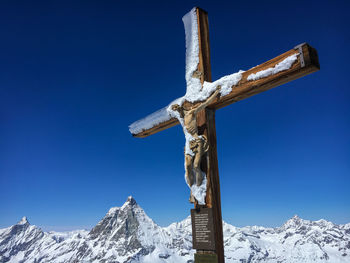 Snow covered cross with figure of jesus christ at peak with matterhorn in the background against blu