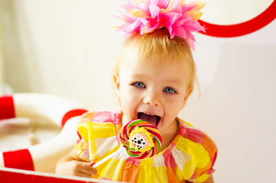 Portrait of happy girl licking lollipop at home