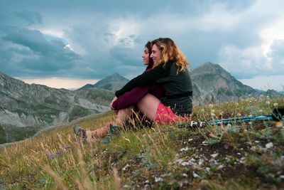 Woman sitting on mountain against sky