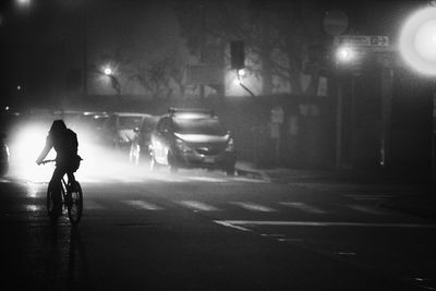 Silhouette man riding bicycle on wet street at night