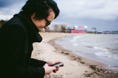 Woman using mobile phone at beach against sky