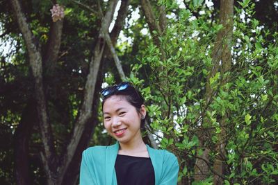 Portrait of smiling young woman standing against trees in forest