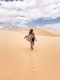 Rear view of woman walking on sand dune in desert against sky