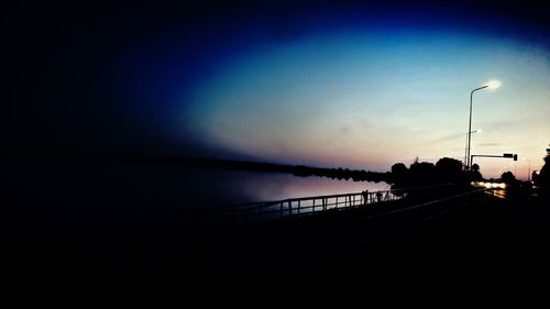 Silhouette street by sea against sky at sunset