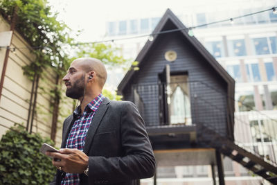 Low angle view of businessman holding smart phone at office yard