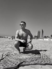 Full length of shirtless man on beach against clear sky