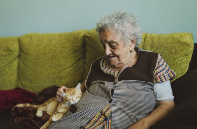 Senior woman sitting on couch stroking tabby cat