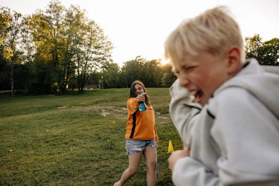 Girl spraying water on male friend while playing in playground at summer camp