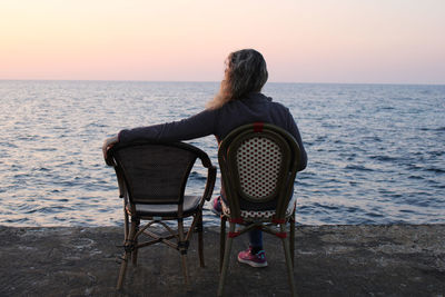 Rear view of woman looking at sea against sky during sunset