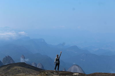 Rear view of man standing on mountain against sky