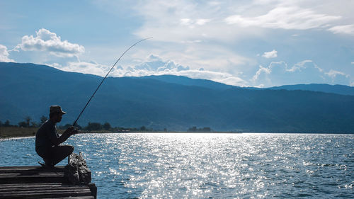 Man fishing in lake against sky