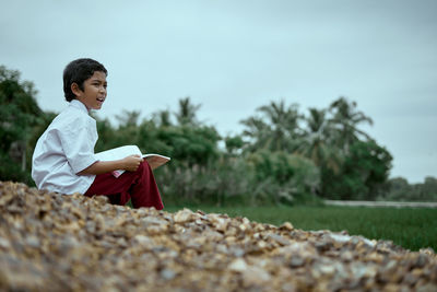 Surface level of boy reading book on field against sky