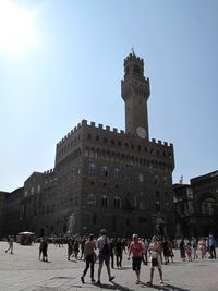 Group of people walking in front of historical building against sky