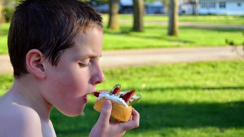 Side view of shirtless boy eating at park