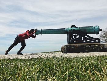 Man pushing cannon against sky