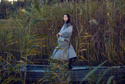 Woman stands in a gray sweater and skirt next to the lake in the fall